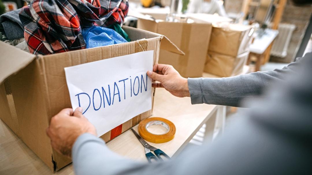 Two people packing a box labeled "donation" with clothes in a room filled with other packed boxes.