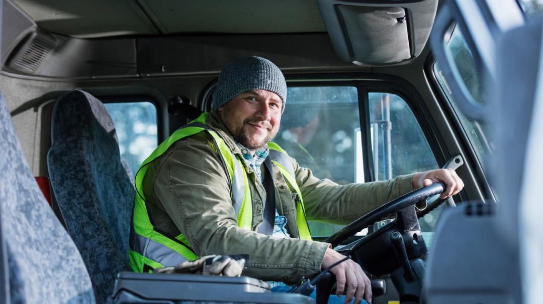 A male truck driver sitting in his truck while holding on to the steering wheel.